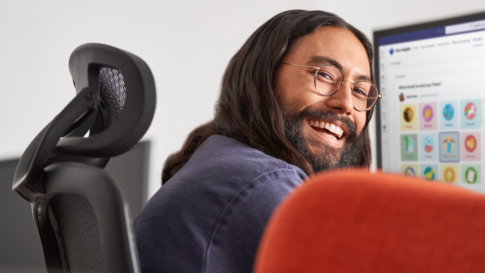 Man smiling while at work​ Keywords: Viva; Filip; hybrid work; work from home; remote; male; desktop monitor; UI screen; glasses; looking back over his shoulder; office; ; Insights; praise