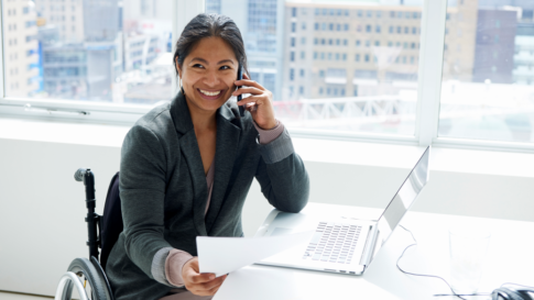 Smiling woman working in office while sitting in wheelchair.