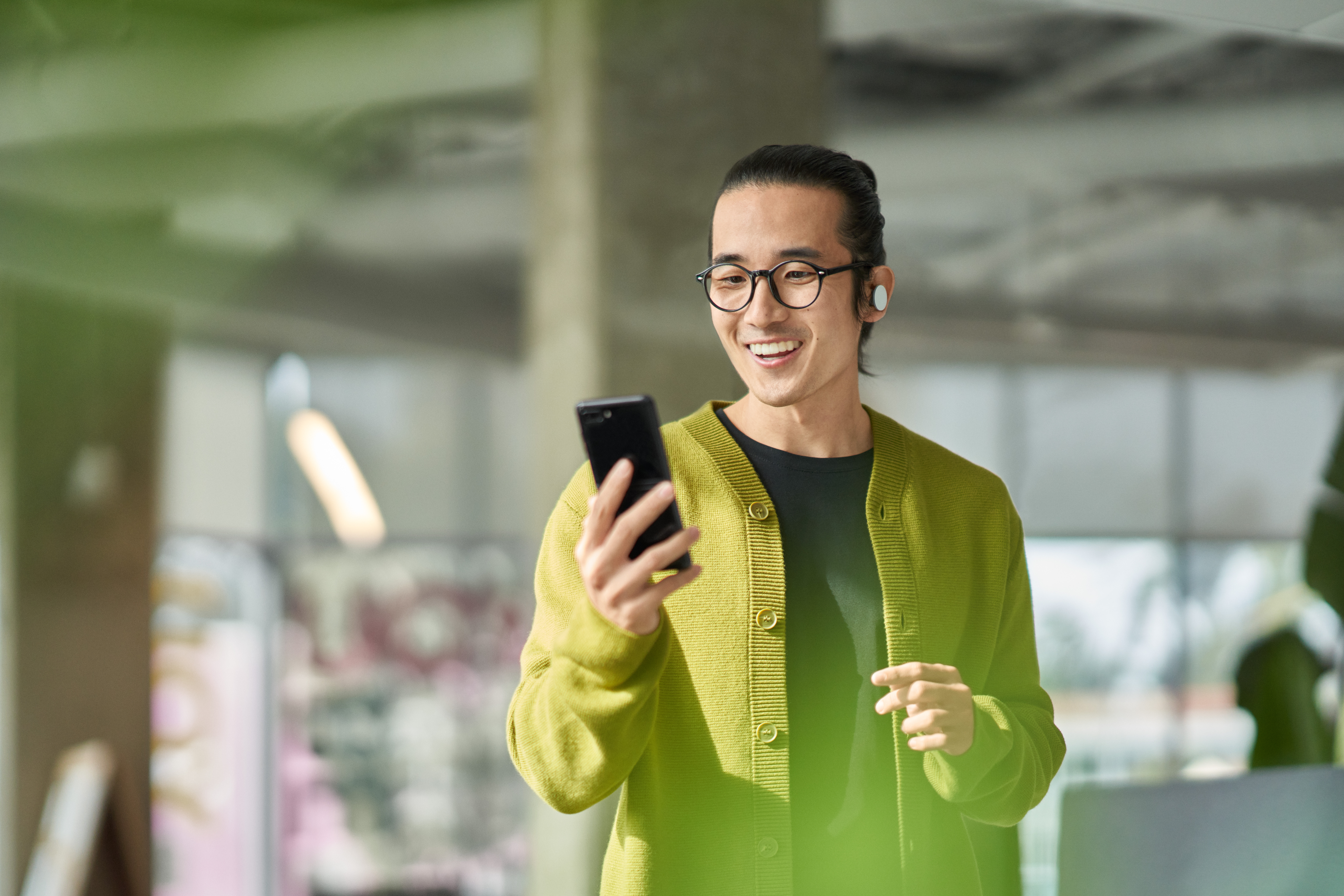 A man collaborating with others during a Microsoft Teams meeting while on the go​. Keywords​: MS Teams; co-working; coworking; male; glasses; mobile phone; device; ear buds; person