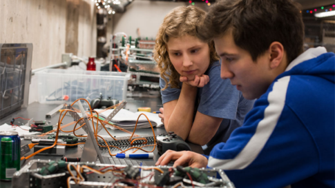 Real people. High school classroom. Two students work together in a robotics lab learning environment. Both stare intently at a computer screen. working about Mlops